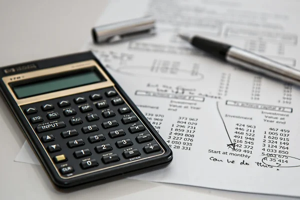 Se realiza la asesoría contable y tributario en un estado financiero. Hay una calculadora, un bolígrafo y el balance en papel.